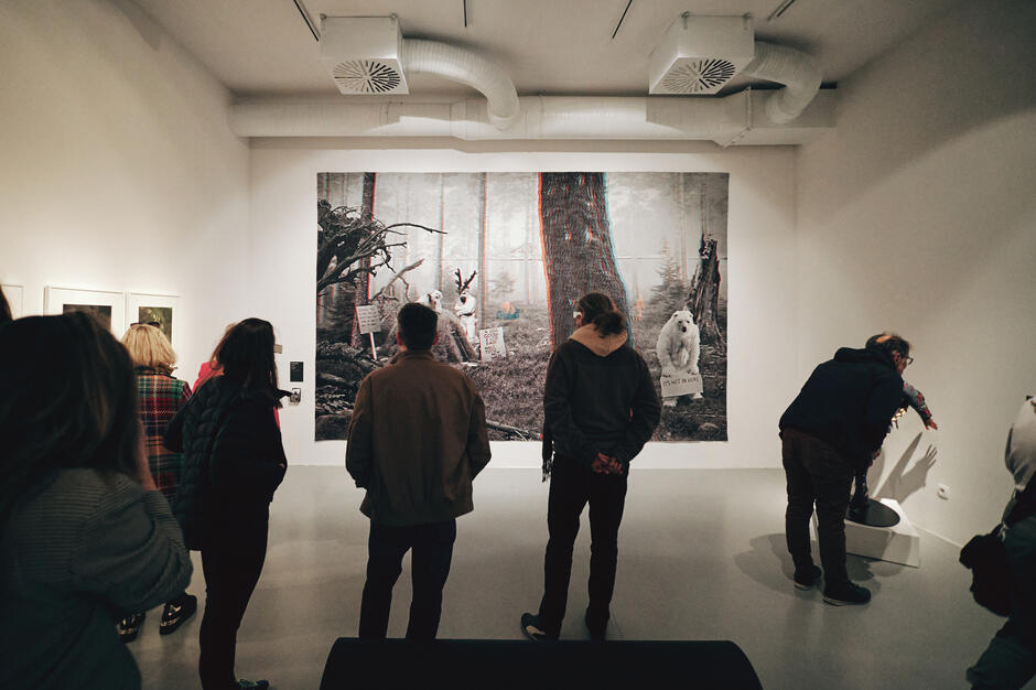 Ludzie stojący tyłem do nas wpatrują się w wielkoformatową fotografię 3D