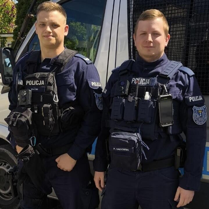 Dwaj policjanci w mundurach patrolowych pozują do zdjęcia, stojąc jeden obok drugiego