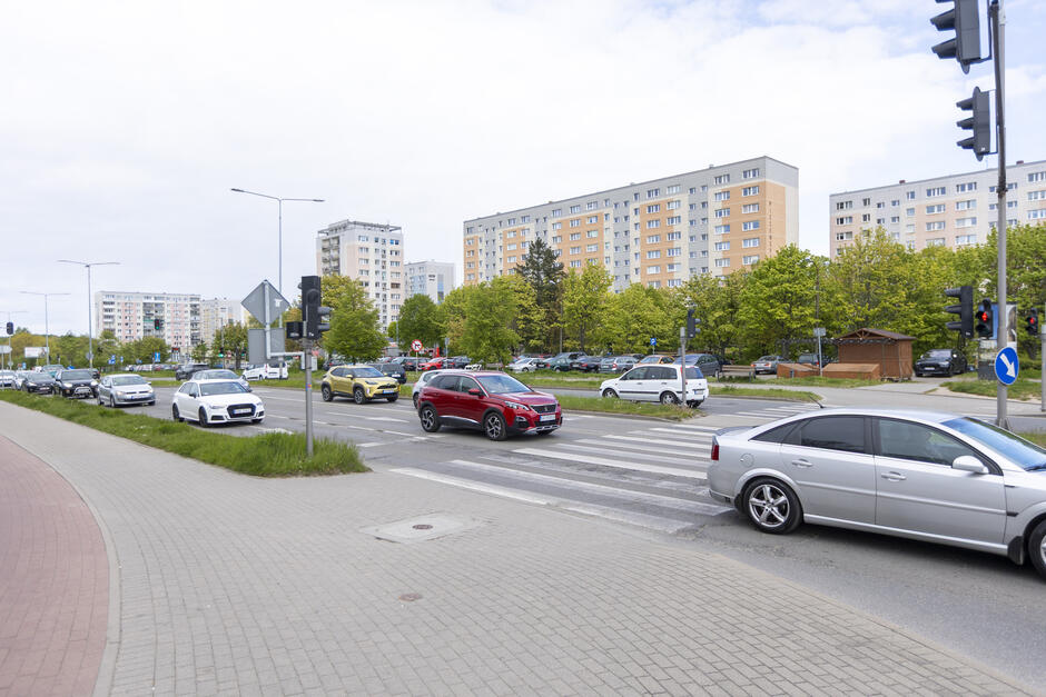 na zdjęciu ulica po której jadą samochody, w tle budynki mieszkalne