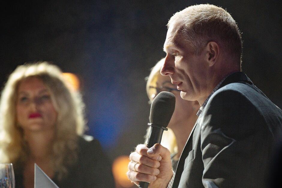 Zdjęcie profilu szczupłego mężczyzny, który siedzi przy stole, mówiąc do mikrofonu