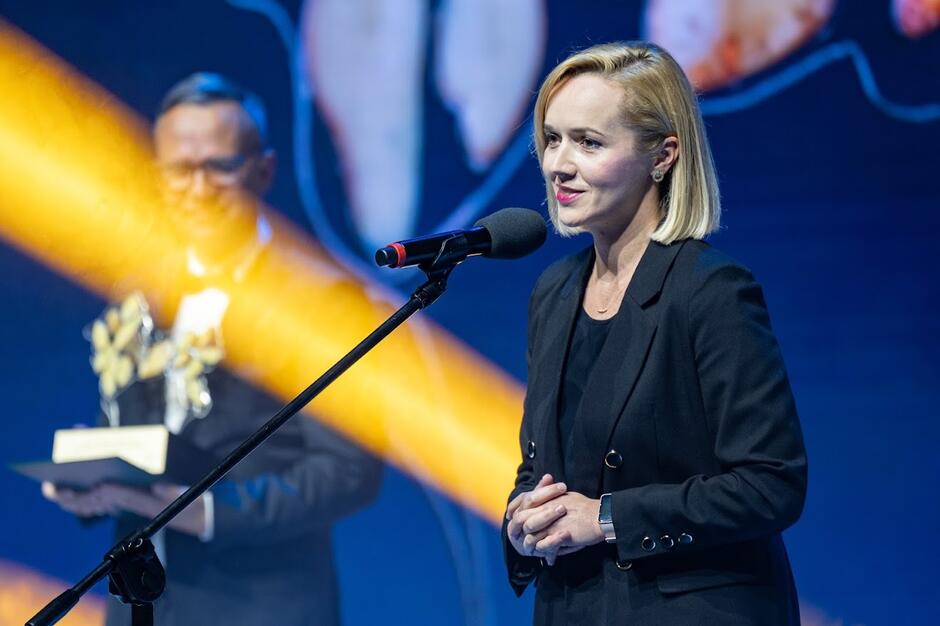 Uśmiechnięta kobieta o długich blond włosach tuż przed odebraniem statuetki