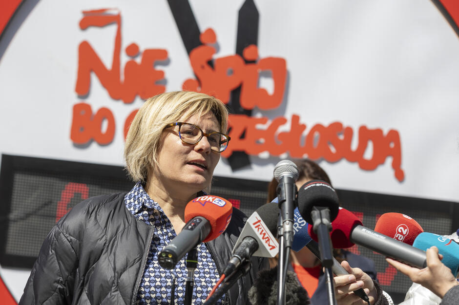 Na trzecim zdjęciu widzimy kobietę przemawiającą do zgromadzonych dziennikarzy podczas tej samej kampanii społecznej „Nie śpij, bo Cię przegłosują”. Stoi przed mikrofonami należącymi do różnych ogólnopolskich mediów (TOK FM, TVN24, Radio Gdańsk, Eska, Zet), co wskazuje na duże zainteresowanie tematem.