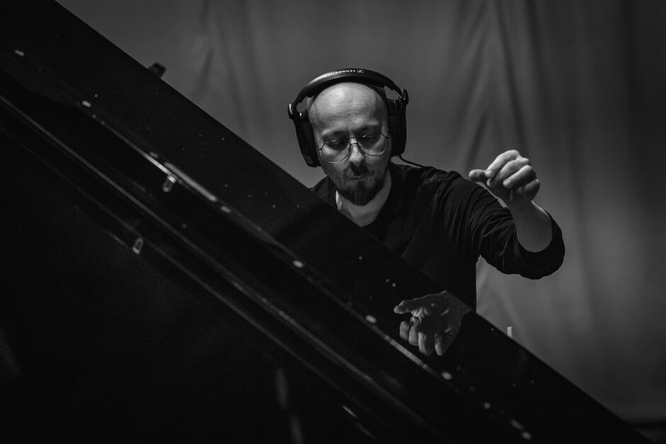 Na zdjęciu osoba w słuchawkach z uniesioną lewą ręką.