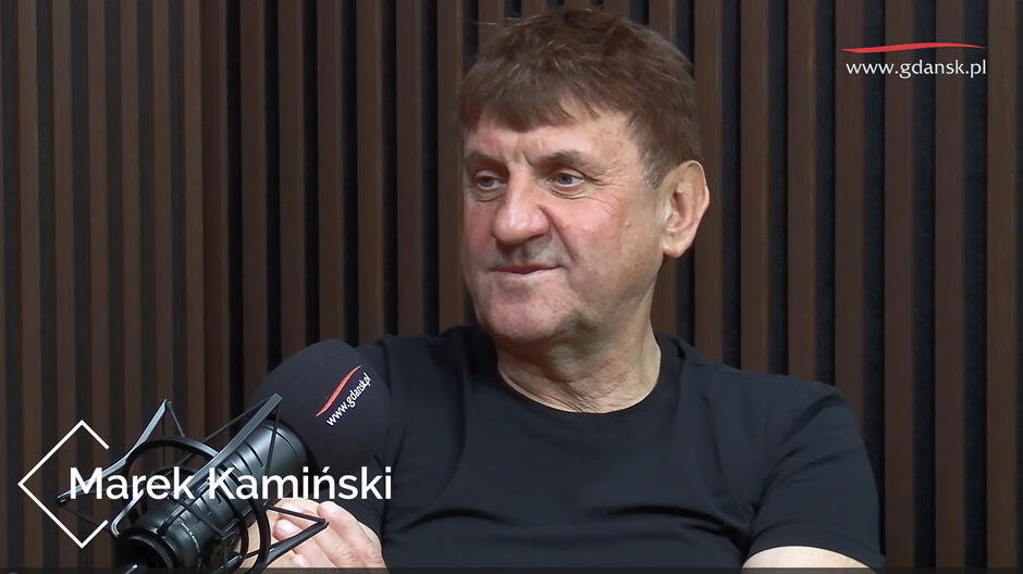Mężczyzna siedzi przed mikrofonem w studiu nagrań.