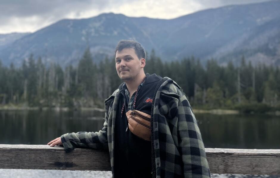 Na zdjęciu młody mężczyzna w koszulki w kratkę na tle gór.