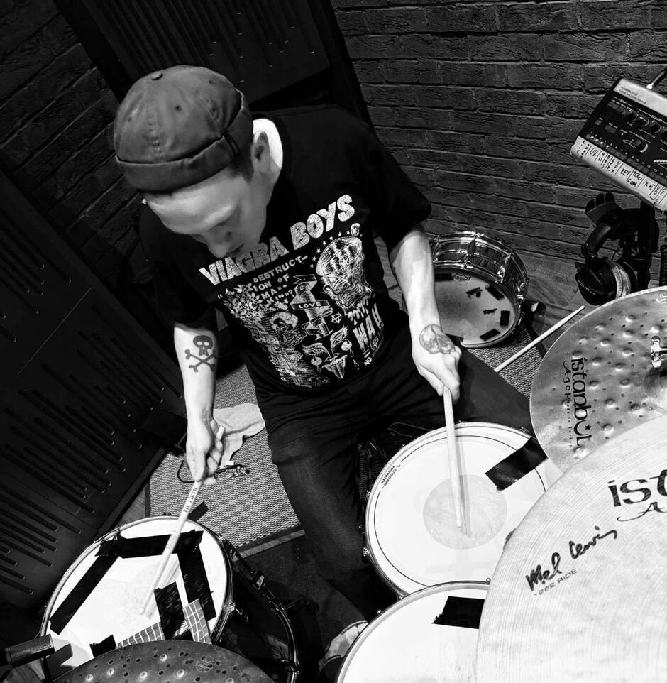 Na zdjęciu znajduje się mężczyzna w czapce z daszkiem, grający na perkusji.