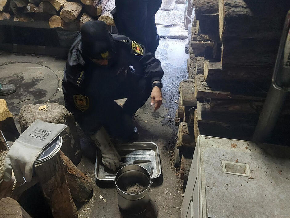 Strażnik miejski klęczy przy piecu, obok którego leży stos drewna do palenia. Fot. Straż Miejska w Gdańsku