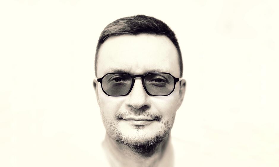 Zdjęcie przedstawia twarz mężczyzny w okularach.