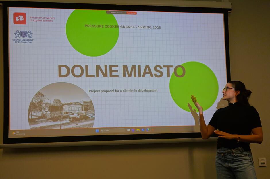 Studentka pokazuje na wielki ekran z prezentacją i napisem Dolne Miasto