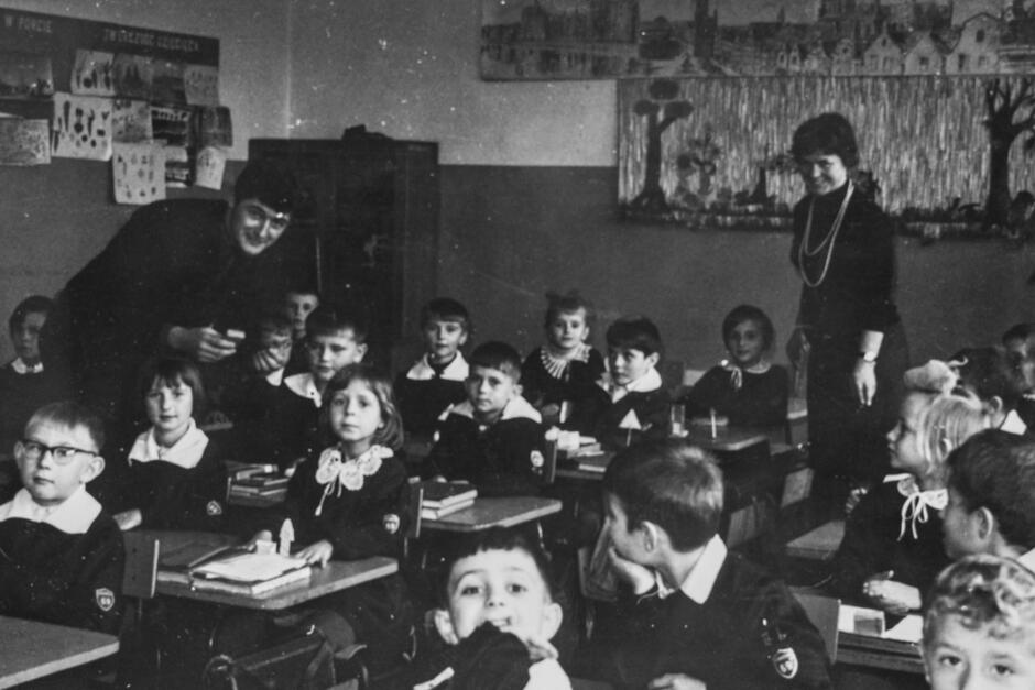 To wyjątkowo sugestywne zdjęcie przedstawia lekcję wczesnoszkolną — najprawdopodobniej w Szkole Podstawowej nr 69 w Gdańsku, wykonane około lat 60. lub początku 70. XX wieku.