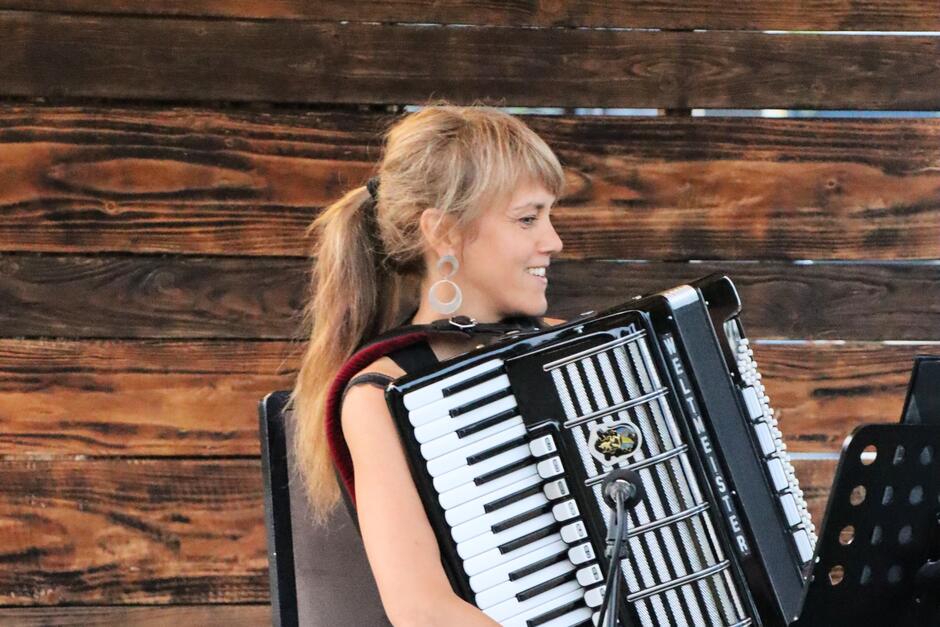 Na zdjęciu kobieta trzymająca akordeon, na tle drewnianej ściany.
