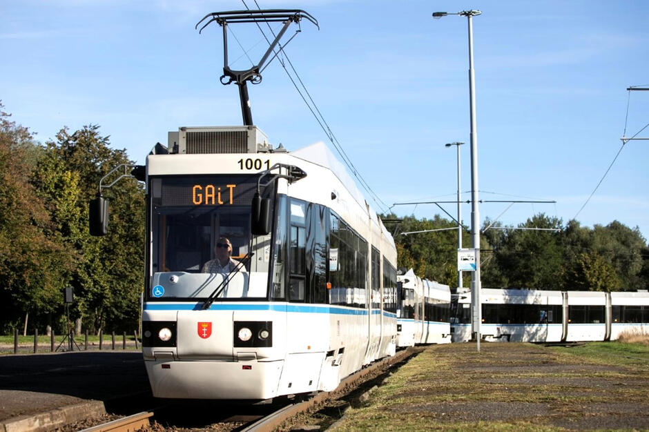 Kremowy tramwaj na torach, wokół drzewa.
