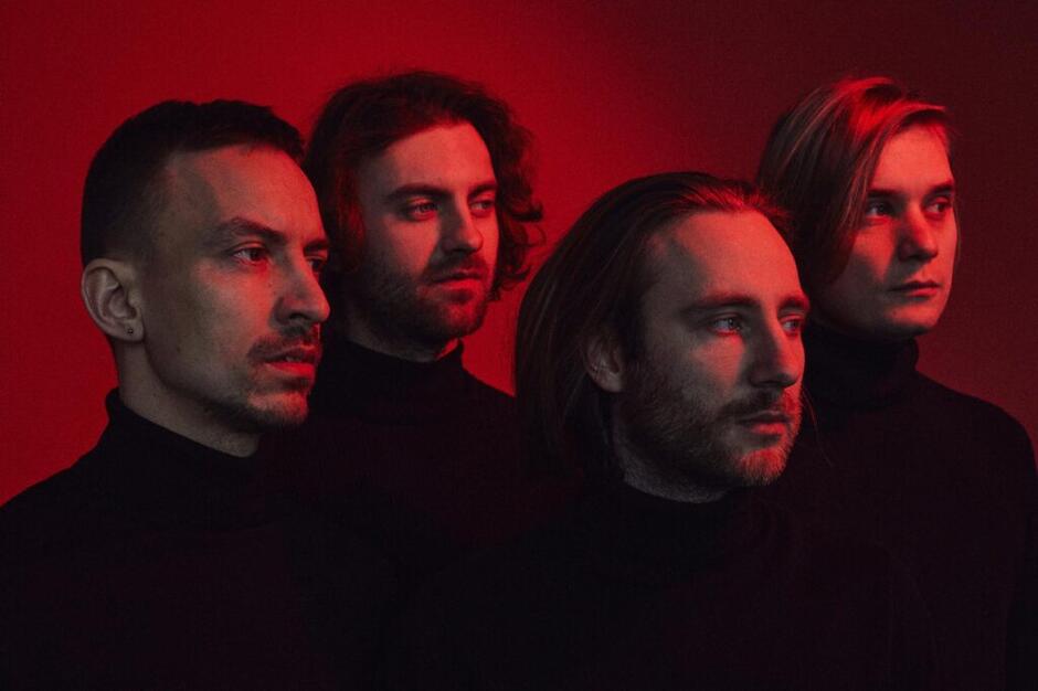 czterech mężczyzn, członków zespołu muzycznego pozuje do fotografii w czerwonym świetle.