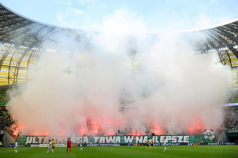 Kibice Lechii Gdańsk odpalają race i tworzą widowiskową oprawę na trybunach, spowijając stadion w gęsty dym.