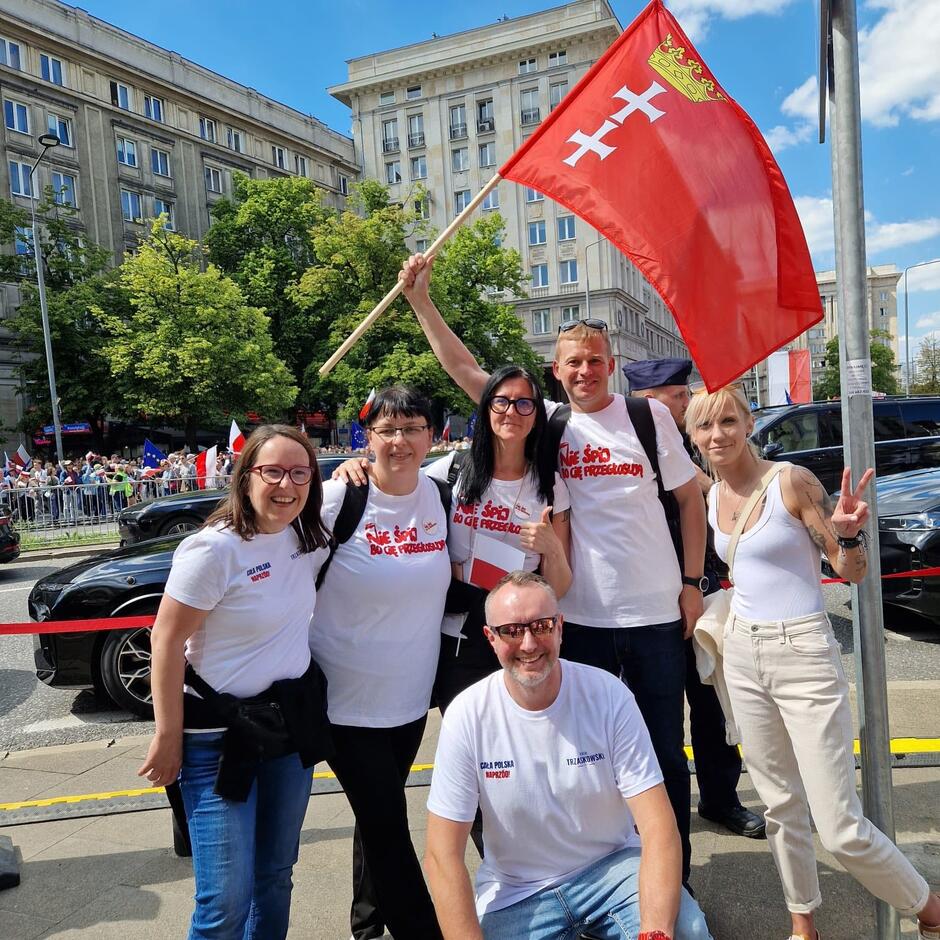 Sześć osób pozuje na ulicy do zdjęcia - jedna z nich, pośrodku, trzyma w ręce flagę Gdańska