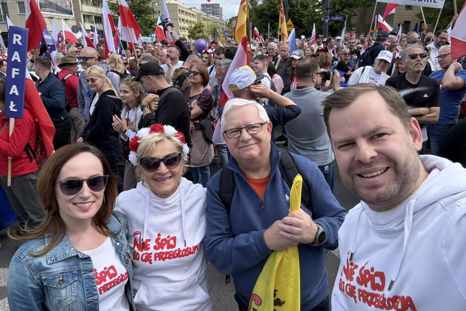 Cztery osoby pozują do selfie na tle tłumu manifestantów