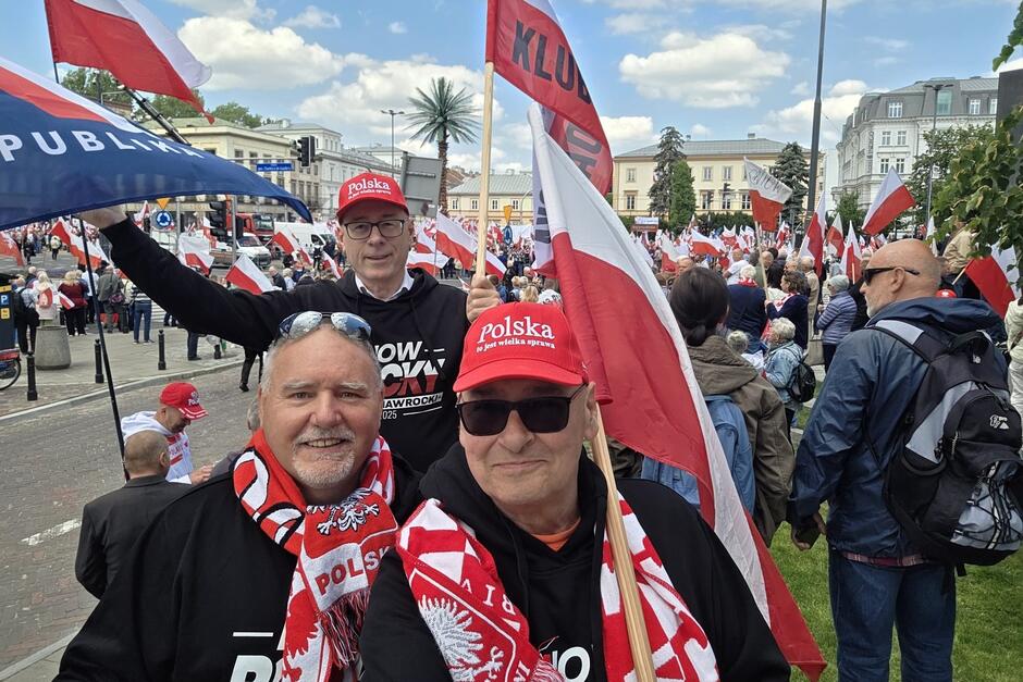 Trzej mężczyźni robią sobie selfie na tle manifestacji