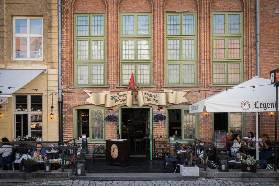 Restauracja w starej, ceglanej kamienicy. Przed lokalem stoją stolika, siedzą ludzie.