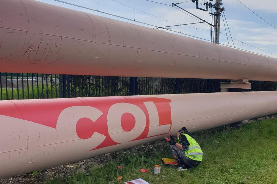 Kucający mężczyzna w roboczym stroju maluje rurę