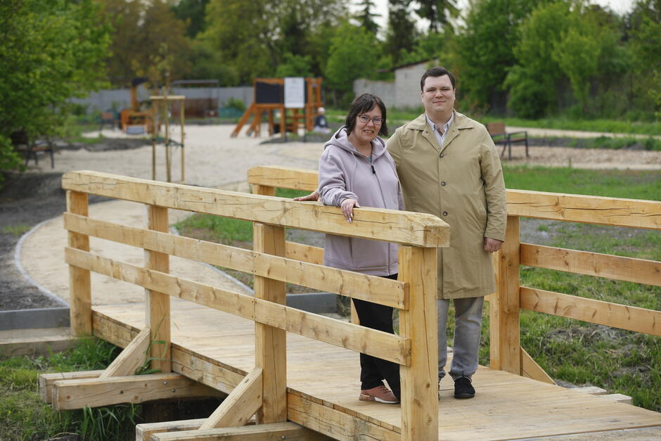 Kobieta i mężczyzna pozują do zdjęcia, stoją przy jasnej drewnianej kładce