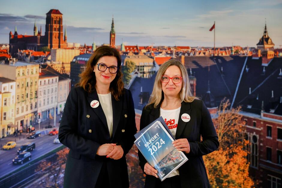 na zdjęciu dwie kobiety w ciemnych garsonkach, pozują do zdjęcia