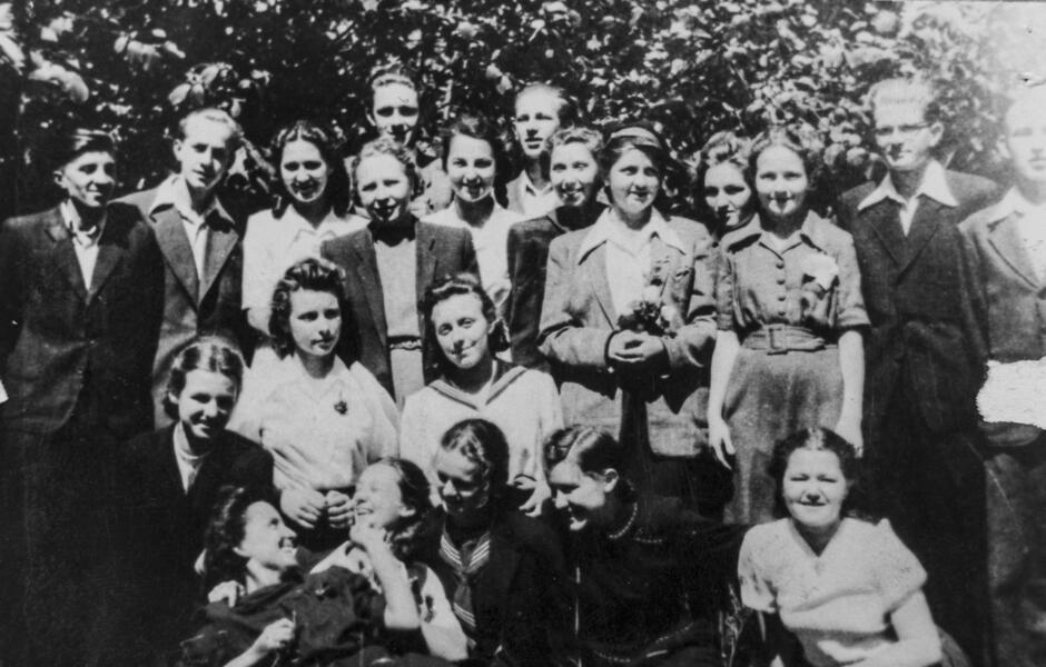 Na zdjęciu widoczna jest czarno-biała fotografia grupowa, najprawdopodobniej zrobiona w pierwszej połowie XX wieku. Widać na niej uczniów i uczennice – być może również nauczycieli – pozujących wspólnie na tle drzew. Osoby są ubrane elegancko, zgodnie z ówczesną modą: marynarki, sukienki, koszule z kołnierzykami. Kilka osób się uśmiecha, panuje dość pogodna atmosfera. Ze względu na styl ubioru oraz jakość zdjęcia można przypuszczać, że fotografia została wykonana w latach 40. lub 50. XX wieku. Biorąc pod uwagę wcześniejsze zdjęcie budynku III LO w Gdańsku,