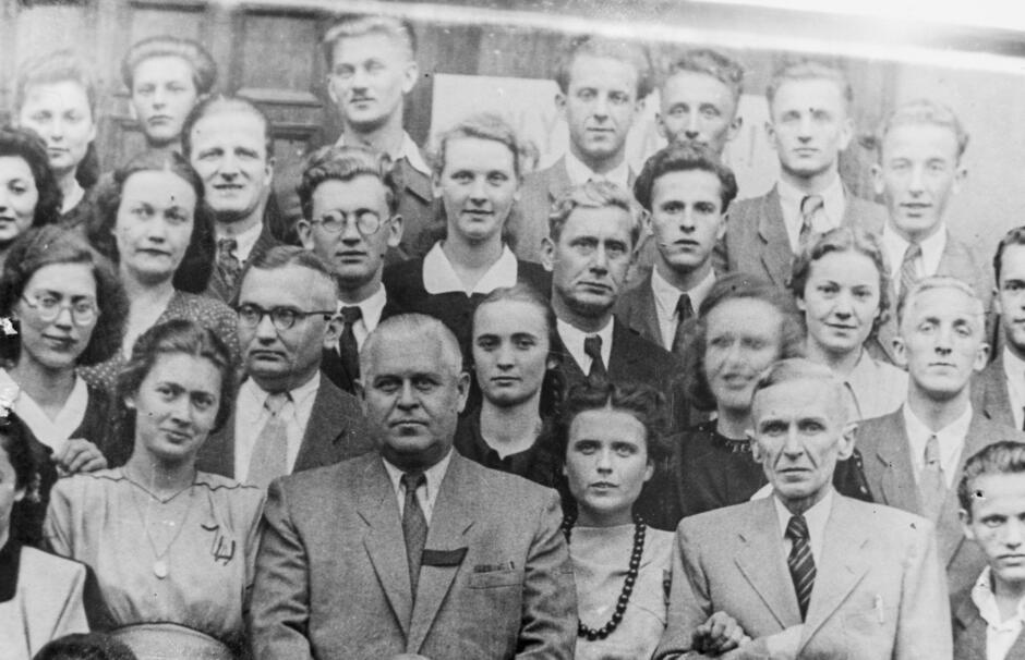 To kolejne archiwalne zdjęcie grupowe, które również prawdopodobnie pochodzi z III Liceum Ogólnokształcącego w Gdańsku. Fotografia jest czarno-biała i przedstawia dużą grupę ludzi – zarówno mężczyzn, jak i kobiety – ustawionych w kilku rzędach, co wskazuje na oficjalny charakter zdjęcia, być może klasowego lub pamiątkowego dla grona pedagogicznego i uczniów.