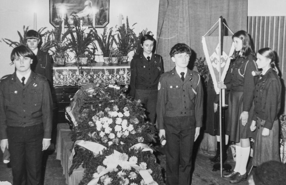 To czarno-białe zdjęcie przedstawia harcerską wartę honorową przy trumnie, co świadczy o ceremonii pogrzebowej osoby związanej ze środowiskiem harcerskim lub szkolnym – prawdopodobnie w III Liceum Ogólnokształcącym w Gdańsku.