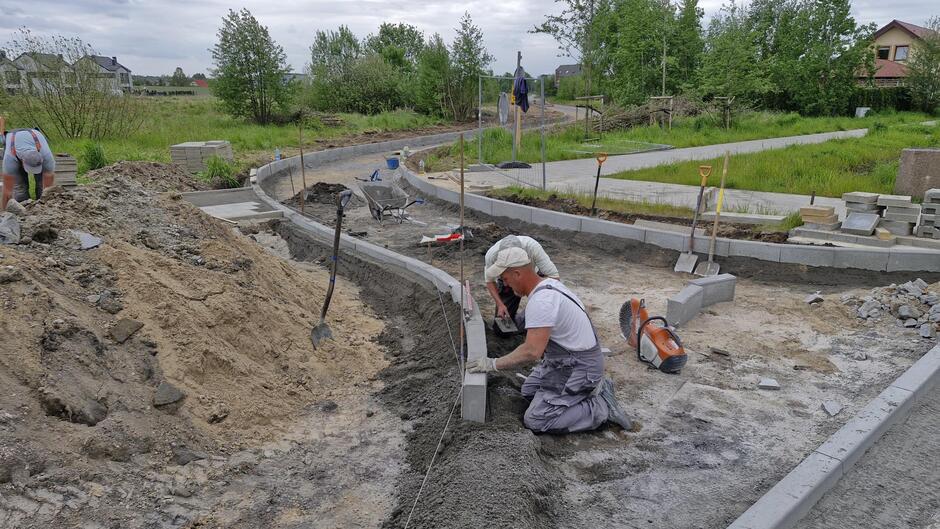 na zdjęciu klękający robotnik, układa krawężnik, w tle widać już spory odcinek nowego krawężnika układany na drodze gruntowej