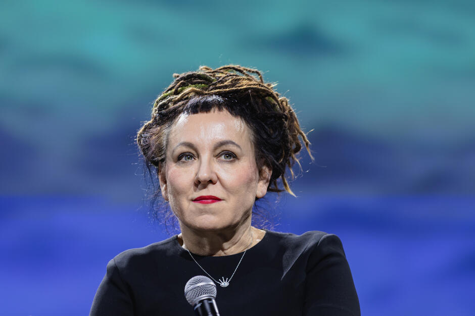 Portret kobiety, pisarki Olgi Tokarczuk z mikrofonem na scenie.