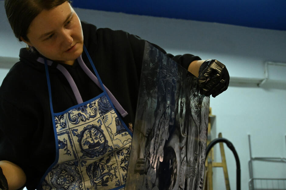 Na zdjęciu kobieta w ciemnej bluzie z brudną od farby ręką.