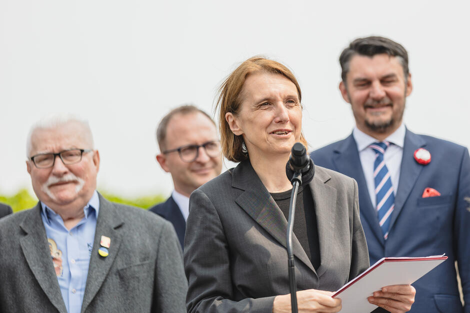 na zdjęciu dojrzała kobieta w krótkich włosach i ciemnej marynarce, mówi do mikrofonu