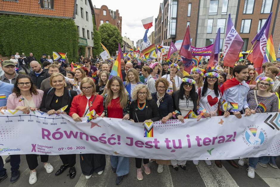 To zdjęcie przedstawia czoło Trójmiejskiego Marszu Równości 2025, który odbył się 7 czerwca. Uczestnicy trzymają baner z hasłem: „Równość! Jest tu i teraz!”, co doskonale oddaje ducha wydarzenia – walki o prawa człowieka, akceptację i szacunek dla różnorodności.
