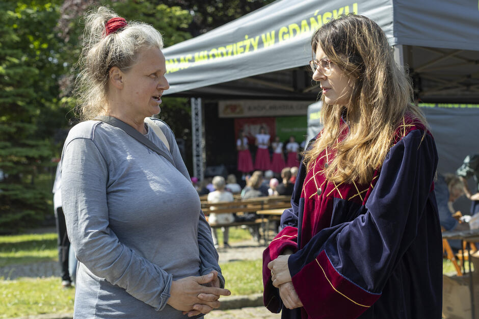 Dwie kobiety stoją w plenerze, rozmawiając - radna w todze jest po prawej stronie zdjęcia