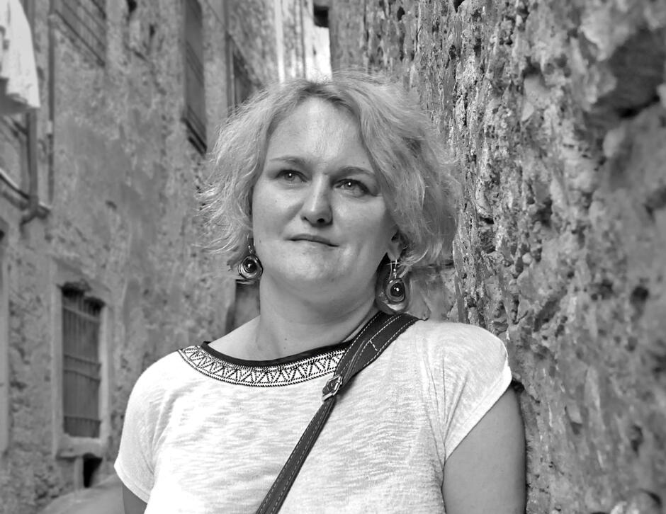 Na czarno-białym zdjęciu kobieta z jasnymi włosami za uszy, ubrana w białą bluzkę.