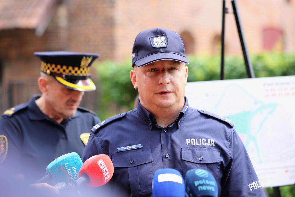 na zdjęciu policjant w mundurze mówiący do mikrofonów dziennikarskich