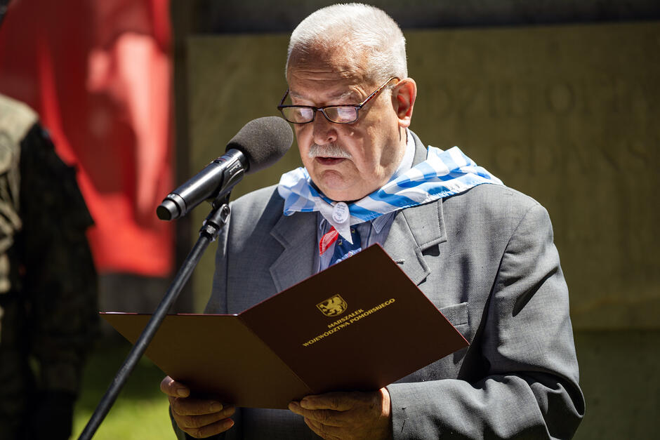 Mężczyzna z chustą obozu koncentracyjnego przemawia na cmentarzu.