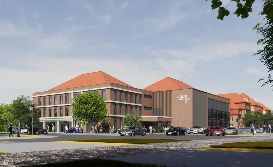 Nowoczesny budynek kompleksu sportowo-rekreacyjnego „Aqua Wrzeszcz” z czerwonymi dachami nawiązuje do architektury okolicznych zabudowań. Przed obiektem widać zaparkowane samochody i spacerujących mieszkańców