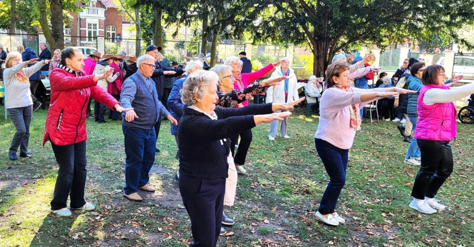 na zdjęciu ćwiczące starsze panie, w plenerze, prawdopodobnie w parku, są w ubraniach z długim rękawem