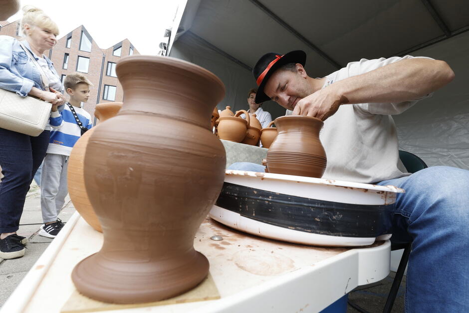 na zdjęciu garncarz siedzi przy stoliku, na pierwszym planie stoi brązowy gliniany wazon