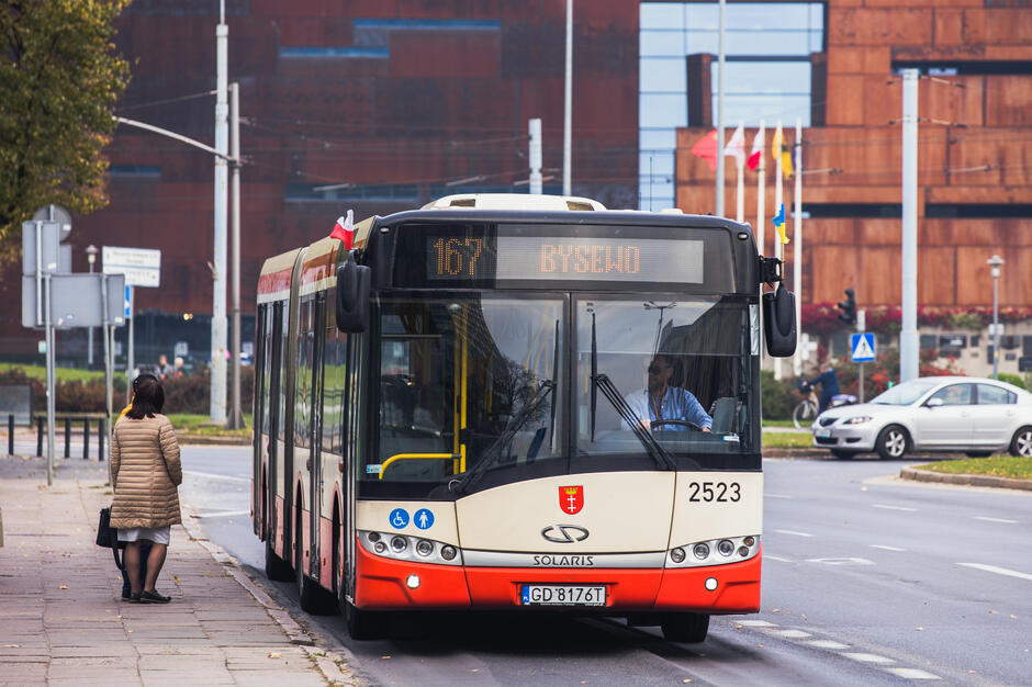 kobieta stoi na przystanku obok autobusu