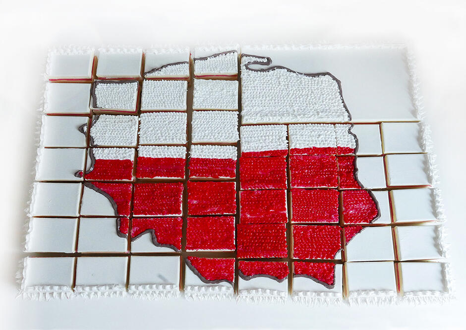 Obraz przedstawia Polskę w formie ciasta podzielonego na kawałki, ozdobionego w barwy narodowe – biało-czerwone. Praca ironicznie komentuje tematy patriotyzmu, konsumpcjonizmu i podziału społeczeństwa