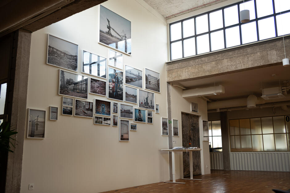 Na ścianie w przestrzeni wystawienniczej wisi kompozycja kilkunastu fotografii o tematyce industrialnej i portowej. Całe pomieszczenie ma surowy, loftowy charakter z wysokimi sufitami i dużymi oknami wpuszczającymi dużo światła.