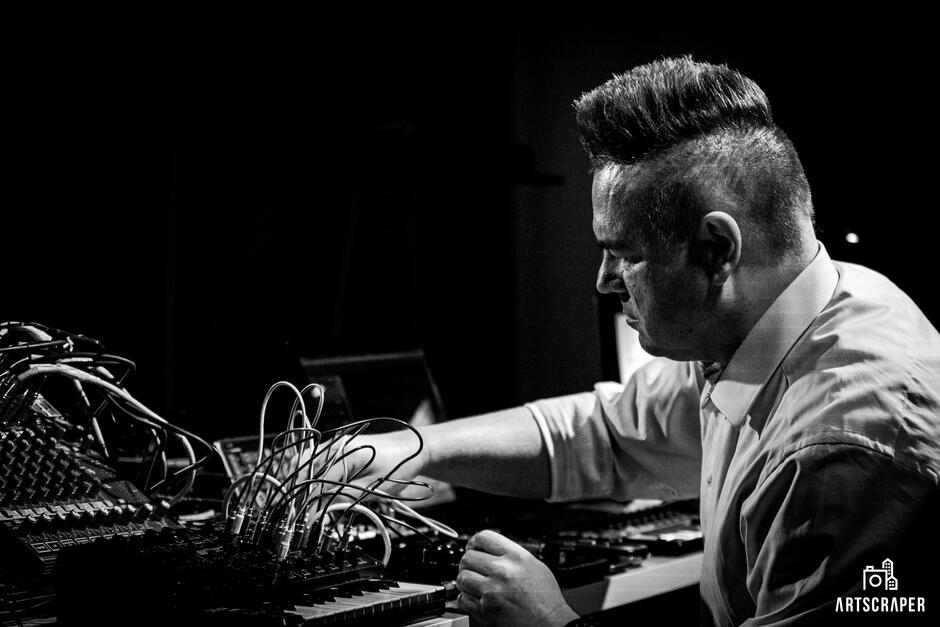 Na zdjęciu mężczyzna przy mikserze do muzyki - przełącza kable.