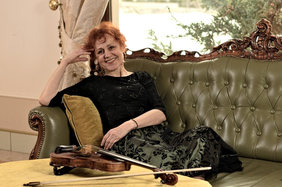 Na zdjęciu kobieta siedząca na kanapie, przed nią na stoliku leżą skrzypce.