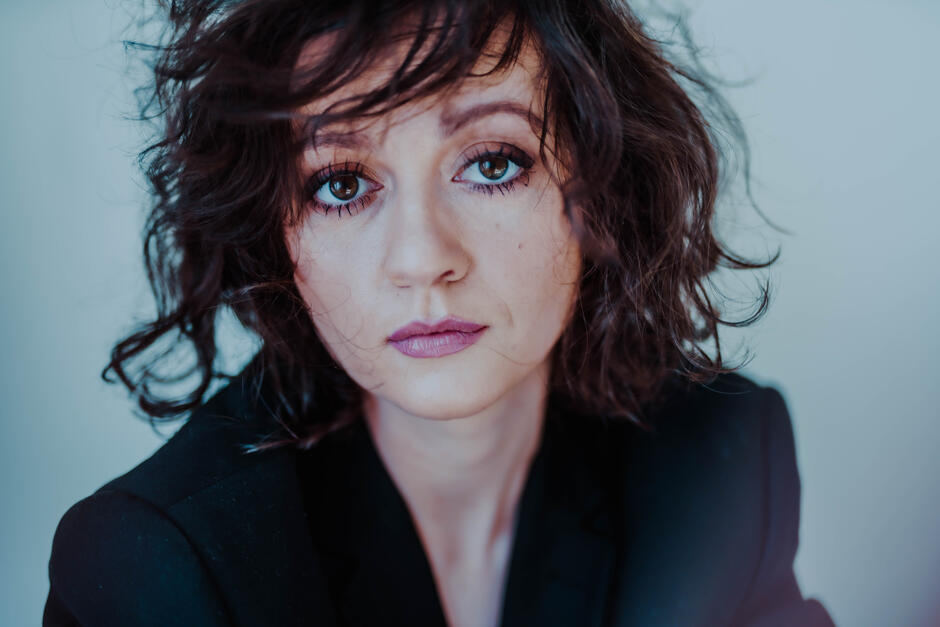 Na zdjęciu kobieta z rozwianymi włosami, na sobie ma ciemną marynarkę.