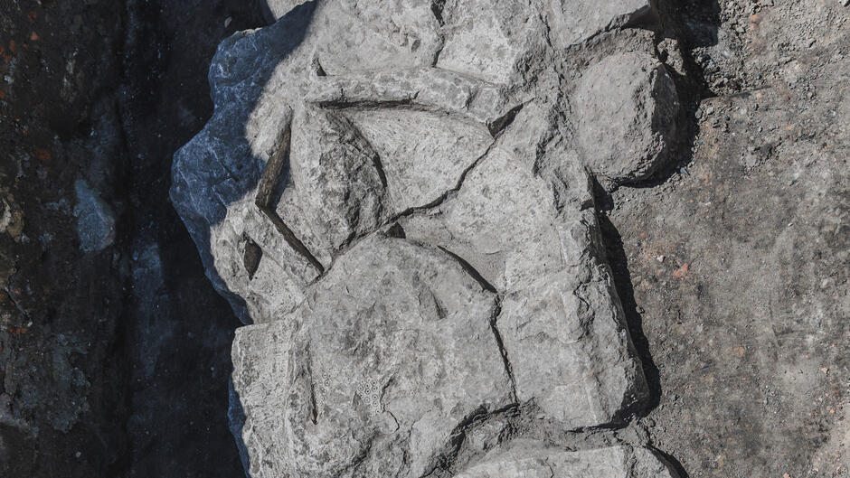 Fragment wykopanego kamiennego reliefu, na którym widać zarys postaci z mieczem. Powierzchnia jest popękana, co sugeruje, że jest to bardzo stary element architektoniczny lub rzeźbiarski.