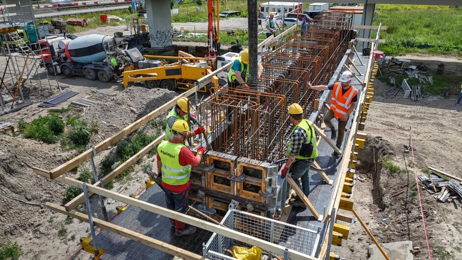na zdjęciu robotnicy stojący przy budowanym filarze mostu, widać druty wystające z betonowego filaru