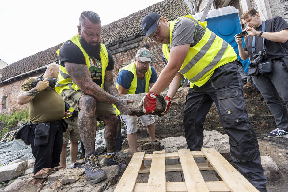 Trzej mężczyźni przenoszą duży płaski blok kamienny