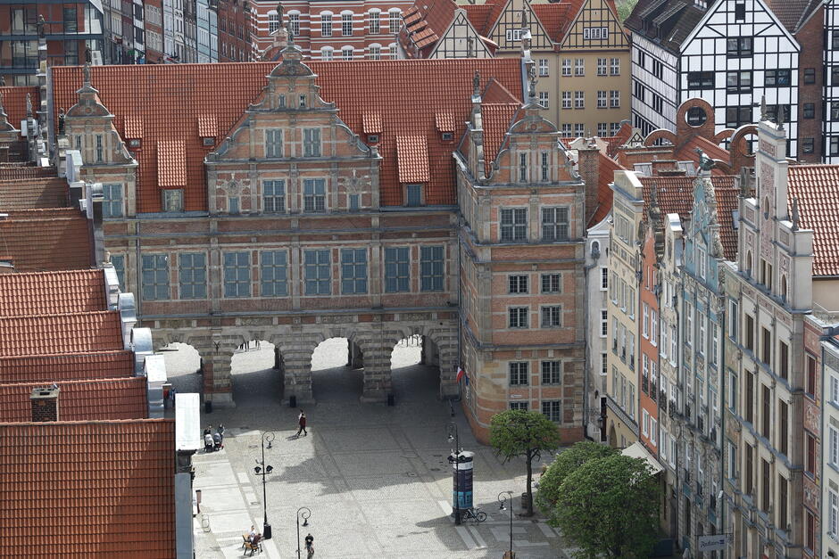 Na zdjęciu widzimy Zieloną Bramę (Brama Zielona) w Gdańsku, znajdującą się na końcu Długiego Targu, tuż przy Moście Zielonym i Motławie. To renesansowy budynek z XVI wieku, pełniący kiedyś funkcję rezydencji dla monarchów. Choć wygląda jak pałac, tak naprawdę jest to brama miejska z przejściem dla pieszych w czterech arkadach. To jedno z najbardziej charakterystycznych miejsc w Gdańsku, często fotografowane przez turystów. Obecnie w budynku mieści się m.in. oddział Muzeum Narodowego i czasami odbywają się tam wystawy